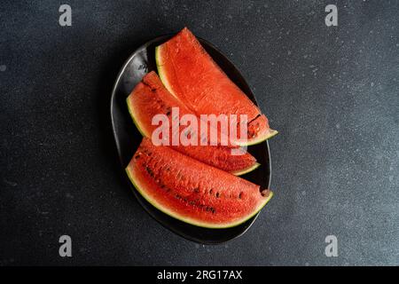 Top view of slices of watermelon served on black plate against dark surface Stock Photo