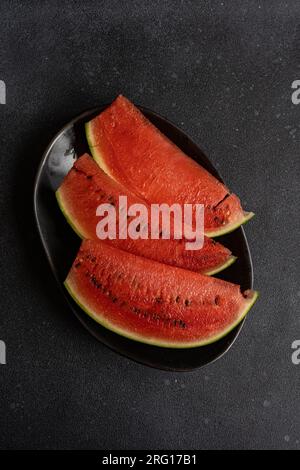 Top view of slices of watermelon served on black plate against dark surface Stock Photo