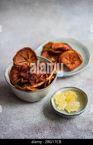 High angle of slices of dried apples and persimmon fruits served in ceramic bowls against blurred gray background Stock Photo