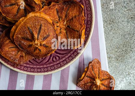 Closeup of slices of dried apples served on ceramic plate on striped napkin against blurred gray background Stock Photo