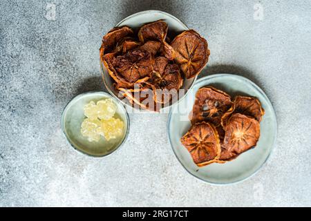 Top view of slices of dried apples and persimmon fruits served in ceramic bowls against blurred gray background Stock Photo