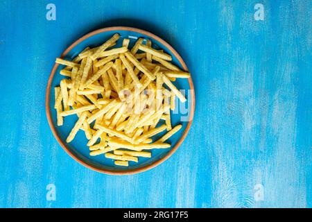 Top view of ceramic plate with French fries placed on blue surface Stock Photo