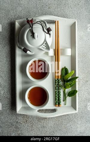 Top view of tea set in Asian style with lemon leaves and chopsticks placed on white tray against gray background Stock Photo