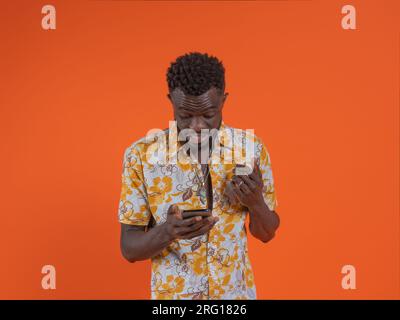 Surprised young African American male in casual outfit looking at screen of mobile phone against orange background Stock Photo