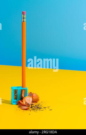 Simple pencil with eraser in plastic sharpener placed on yellow table near shavings against blue wall Stock Photo