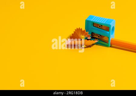 Simple crop pencil in plastic sharpener placed on yellow table near shavings Stock Photo