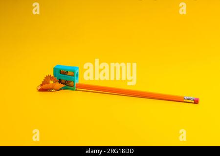 Simple pencil with eraser in plastic sharpener placed on yellow table near shavings Stock Photo