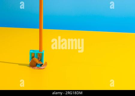 Simple crop pencil in plastic sharpener placed on yellow table near shavings against blue wall Stock Photo