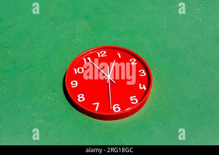 From above big round red clock against green wall background Stock Photo