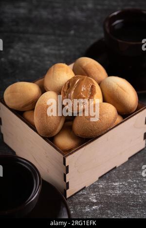 photo wooden box with nuts with boiled condensed milk and two coffee cups, fresh , sweet dessert, homemade, shortbread cookies, on a dark background Stock Photo