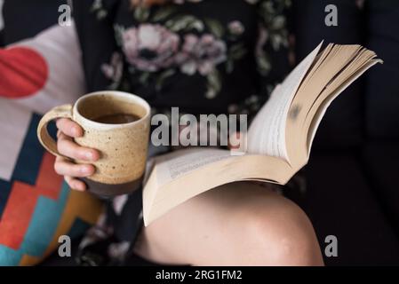 Closeup of woman reading book and holding coffee cup Stock Photo