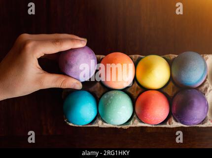 High angle of hand placing dyed egg with other colored Easter eggs. Stock Photo