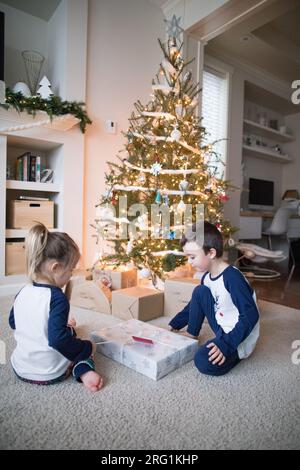 Brother and sister opening gifts together under the tree Stock Photo