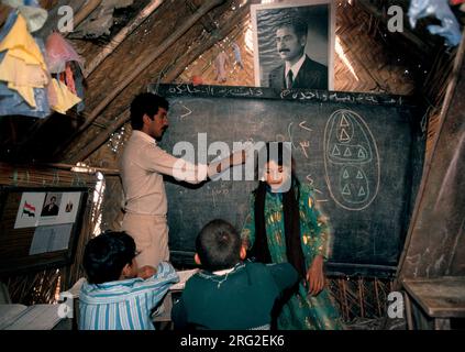 Marsh Arabs Southern Iraq.  Marsh Arab children in school a traditional reed constructed building. Portrait of Saddam Hussein hanging from wall. Rivers Tigris and Euphrates wetlands, Hammar marshes. Southern Iraq 1980s 1984 HOMER SYKES Stock Photo