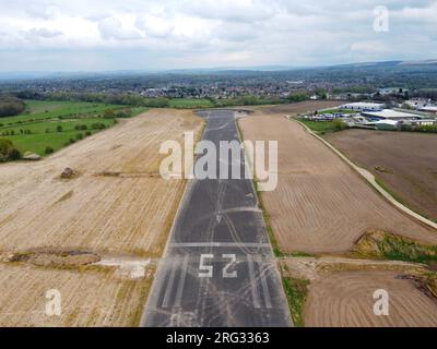 Overhead aerial view of the remaining section of runway 25 of Woodford Aerodrome, United Kingdom with industrial buildings and the town of Poynton in Stock Photo