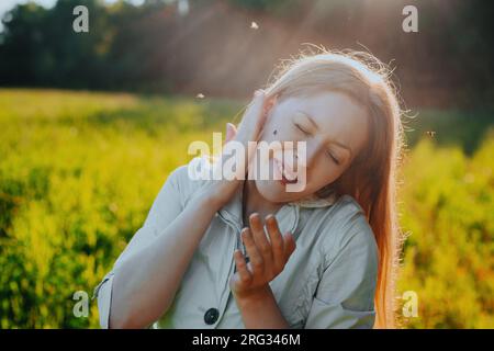 Young woman tries to kill a mosquito on her cheek Stock Photo