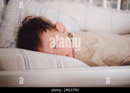 The two-year-old toddler baby is sleeping in his crib. Child boy is sleeping on a pillow in bed. Kid aged two years Stock Photo
