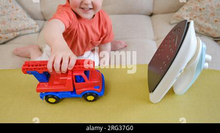 The baby must refrain from playing with a hot iron in the living room due to the potential danger it poses. Children need to be carefully monitored to Stock Photo