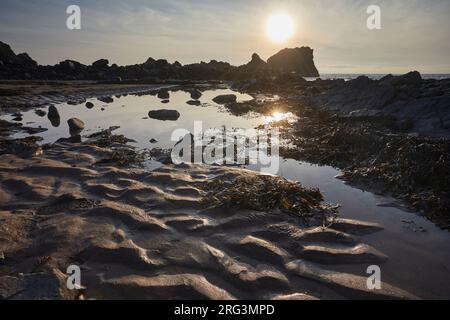 Sunset over a shore at low tide, showing rippled sand, a rock pool and rocks, at Hartland Quay, Hartland, Atlantic coast of Devon, Great Britain. Stock Photo