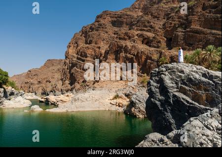 A man looking out over a natural pool in Wadi Al Arbeieen. Wadi Al Arbeieen, Oman. Stock Photo