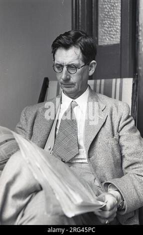 1950s, historical, a gentleman wearing a jacket & tie sitting in a deckchair outside on a porch of a house reading a newspaper, England IUK. Stock Photo
