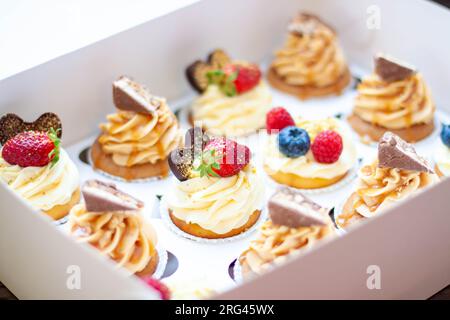 Assorted cupcakes in gift box with fresh strawberries, peanut butter, slated caramel, chocolate, raspberry, strawberry and blueberry Stock Photo