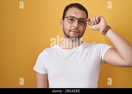 Hispanic man holding glasses thinking attitude and sober expression looking self confident Stock Photo