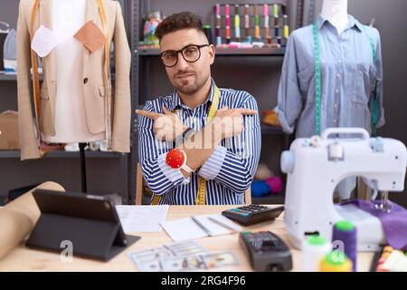 Hispanic man with beard dressmaker designer working at atelier pointing to both sides with fingers, different direction disagree Stock Photo