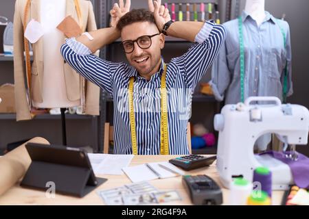 Hispanic man with beard dressmaker designer working at atelier posing funny and crazy with fingers on head as bunny ears, smiling cheerful Stock Photo