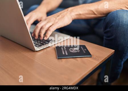 Middle age man using laptop sitting on table with italian passport at home Stock Photo