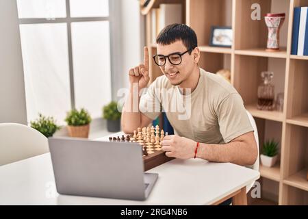 Young arab man playing chess online smiling with an idea or question pointing finger with happy face, number one Stock Photo