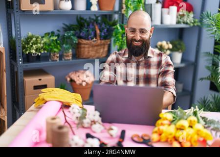 Young bald man florist smiling confident using laptop at flower shop Stock Photo