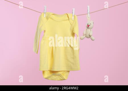 Yellow baby dress and crochet toy drying on washing line against pink background Stock Photo