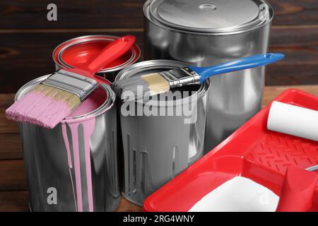 Cans of paints, brushes and tray with roller on wooden table, closeup Stock Photo