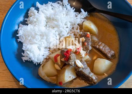 Beef massaman curry made with slow cooked beef, spices and potatoes, garnished with peanuts and chilis and served with Basmati rice. Stock Photo