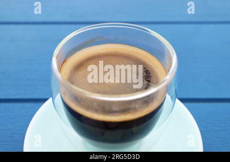 Closed up a glass of hot black coffee isolated on blue wooden table Stock Photo
