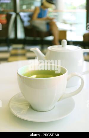 Closeup of a cup of green tea with tea kettle on the table Stock Photo