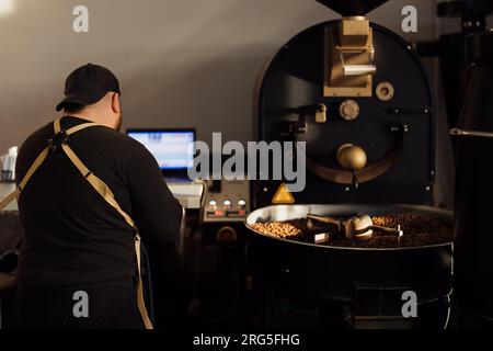 Man using laptop while working with coffee roasting machine Stock Photo