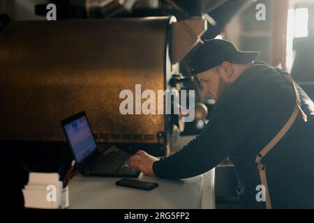 Man using laptop while working with coffee roasting machine Stock Photo