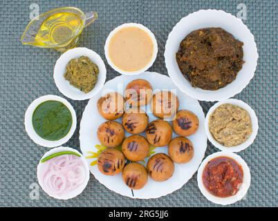 Litti in white plate with tomato, brinjal, potato, pointed gaurd and coriander chutney or chokha and ghee. It is popular in Bihar, Uttar Pradesh Stock Photo