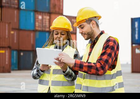 Industrial workers using computer tablet for container shipping control at warehouse storage outdoor - Delivery site concept - Focus on senior African Stock Photo