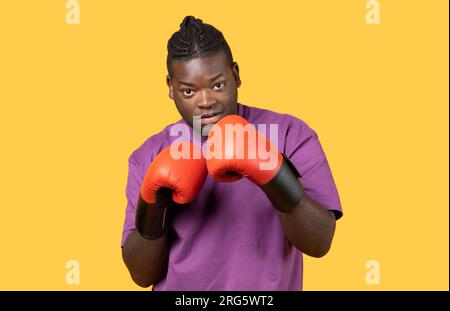 Confident young black boxer man wearing boxing gloves, yellow background Stock Photo