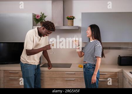 Two young men having a glass of wine in their kitchen while laughing together. Concept: lifestyle, toast, together. Stock Photo