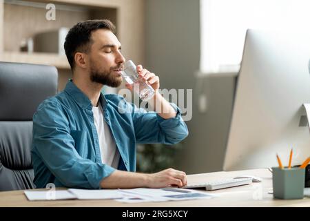 Young Businessman Drinking Water From Glass While Working At Desk In Office Stock Photo
