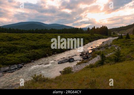 Sun setting over flowing river in the foot hills of the mountains Stock Photo