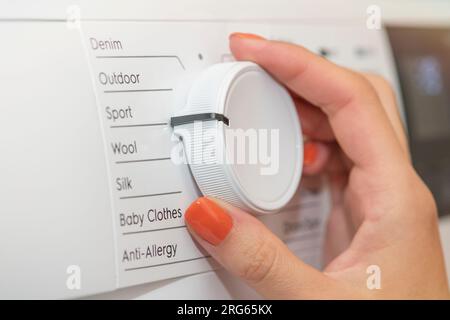The woman turns on the washing machine and adjusts the duration of the wash. Washing dirty clothes in the washing machine. Hands turning on the Stock Photo