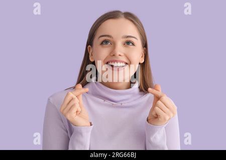 Young woman in sweater snapping fingers on lilac background, closeup Stock Photo