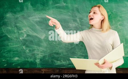 High school teacher near chalkboard in classroom. Happy female teacher giving lesson to students in school or university. College student girl or Stock Photo