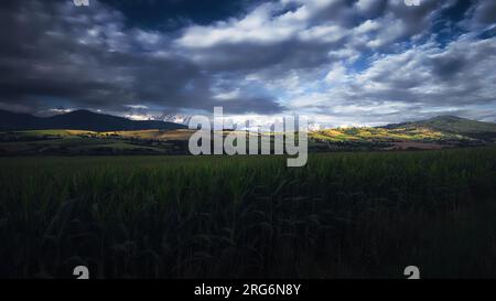Dramatic landscape of hills behind the town of Brezno illuminated by sunlight breaking through heavy clouds, Slovakia Stock Photo