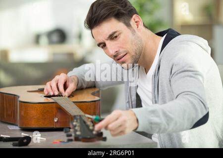 luthier tune guitar strings with peg winder Stock Photo